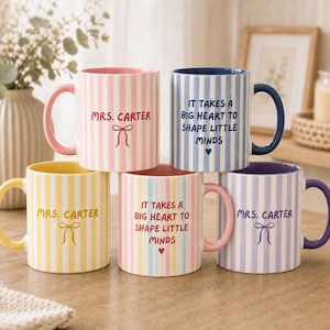 Può includere: Cinque tazze in ceramica con strisce verticali in colori pastello. Tre tazze riportano la scritta 'MRS. CARTER' con l'icona di un fiocco. Due tazze riportano la scritta 'IT TAKES A BIG HEART TO SHAPE LITTLE MINDS' con un piccolo cuore.
