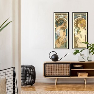 May include: Two framed art prints of women in vintage style dresses with floral accents. The prints are hanging on a white wall above a wooden cabinet with a woven rattan front.