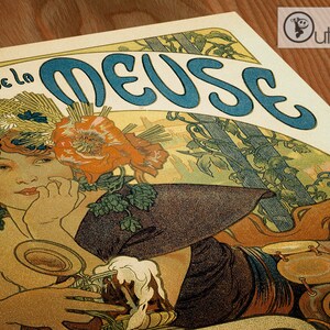 Op de afbeelding: Een vintage poster met een vrouw met een bloemenkrans en een vloeiende jurk, die een glas bier vasthoudt. De poster heeft de titel "Les de la Meuse" en is uitgevoerd in blauw en wit.