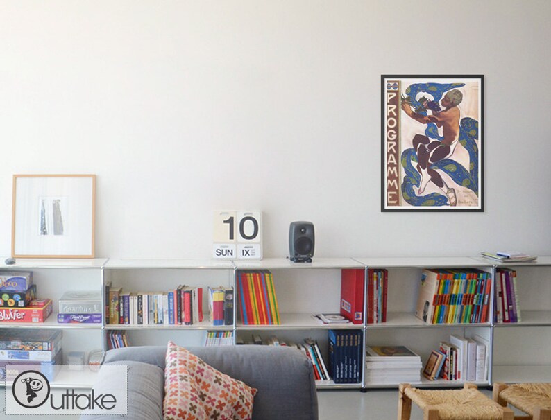 May include: A framed vintage poster with the word "PROGRAMME" vertically on the left side. The poster features a nude figure intertwined with blue and green paisley-patterned serpents. The poster is displayed above a white shelf with books and decorative items.