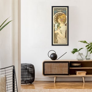 May include: A framed art print of a woman in a white dress holding a bouquet of flowers. The print is in a black frame and is hanging on a white wall. The woman is surrounded by a decorative floral border.