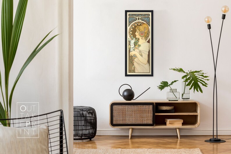 May include: A framed art print of a woman in a white dress holding a bouquet of flowers. The print is in a black frame and is hanging on a white wall. The woman is surrounded by a decorative floral border.