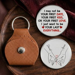 May include: A brown leather keychain with a silver ring and a silver snap. Two round silver tokens with text and illustrations are also present. One token reads "I may not be your first date..." and the other depicts hands holding a heart with the names "David" and "Anna".