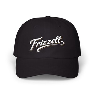 Pode incluir: Boné de beisebol preto com a palavra "Frizzell" bordada em escrita branca com contorno dourado. O boné tem uma aba curva e um ajuste estruturado, adequado para uso casual.