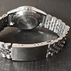 May include: A silver-toned Citizen watch with a stainless steel band. The watch band is a linked design with a clasp that reads "Citizen". The watch face is not visible in this image.
