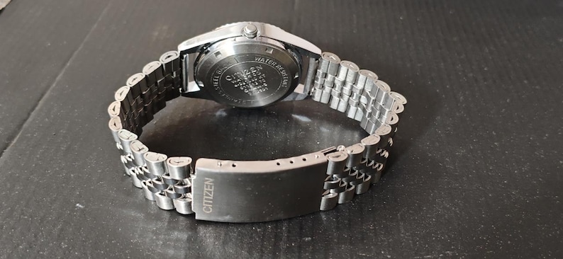 May include: A silver-toned Citizen watch with a stainless steel band. The watch band is a linked design with a clasp that reads "Citizen". The watch face is not visible in this image.