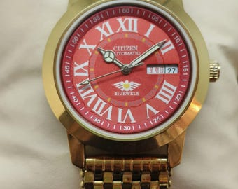 Orologio da uomo automatico Citizen con quadrante rosso, datario e finitura dorata.