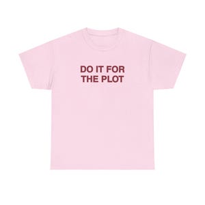 Könnte beinhalten: Ein hellrosa T-Shirt mit kurzen Ärmeln und dem Text DO IT FOR THE PLOT in dunkelroter Farbe mittig auf der Brust. Das Kleidungsstück hat einen Rundhalsausschnitt, eine Standardpassform, kurze Ärmel und einen geraden Saum.