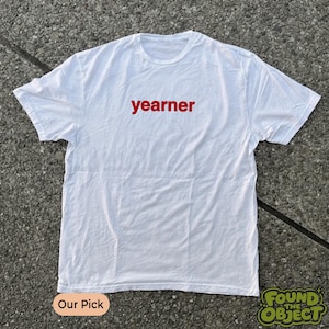 Puede incluir: Una camiseta blanca de manga corta con la palabra yearner impresa en letras minúsculas de color rojo intenso en el centro del pecho. La prenda tiene un cuello redondo estándar y un dobladillo recto, confeccionada en tela blanca.