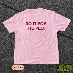 Könnte beinhalten: Ein hellrosa T-Shirt mit kurzen Ärmeln und dem Text DO IT FOR THE PLOT, der in dunkelroten Großbuchstaben mittig auf der Brust aufgedruckt ist. Das Kleidungsstück hat einen Rundhalsausschnitt und eine Standardpassform mit schlichtem Design.