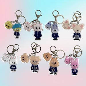 Puede incluir: Ocho llaveros con personajes de animales de dibujos animados. Cada llavero tiene un anillo y un cierre plateados. Los personajes son de color azul, blanco, rosa y beige, y visten chaquetas azul oscuro.