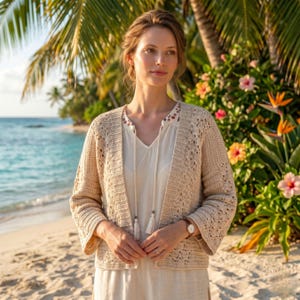 Op de afbeelding: Een beige, opengebreid vest met driekwart mouwen. Het vest wordt gedragen over een witte blouse met een V-hals en kwastjes. De achtergrond toont een strandscène met palmbomen en kleurrijke bloemen.