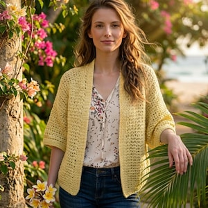 May include: A light yellow crochet cardigan with three-quarter sleeves. The open-front sweater is worn over a floral print blouse and blue jeans. The woman is holding a bouquet of yellow and white flowers.