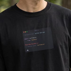 May include: Black t-shirt with a graphic of a code snippet. The code snippet includes the text "import confidence from 'reware'" and "ModuleNotFoundError". The t-shirt is made of a soft material.