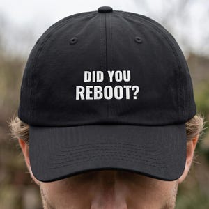 May include: A black baseball cap featuring the white embroidered text DID YOU REBOOT? centered on the front panel. The cap has a structured crown, a curved brim, and a button at the top, constructed from a solid black fabric with matching stitching.