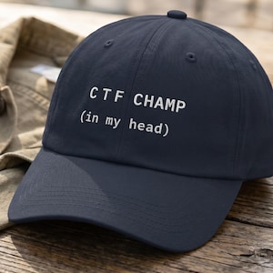 May include: A navy blue baseball cap with the text "CTF CHAMP (in my head)" in white. The cap is sitting on a wooden surface next to a tan jacket.