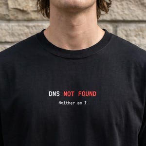 May include: Black t-shirt with the text "DNS NOT FOUND" in red and "Neither am I" in white. The shirt is made of a soft material and has short sleeves.