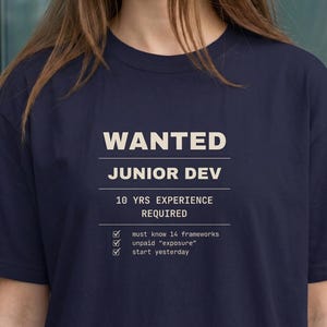 Peut inclure: Un t-shirt bleu marine à manches courtes avec le texte WANTED JUNIOR DEV, 10 YRS EXPERIENCE REQUIRED, et une liste à cocher avec les éléments must know 14 frameworks, unpaid exposure, et start yesterday imprimés en crème sur le devant.