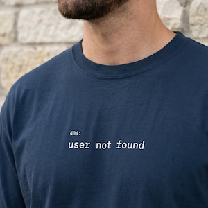 Könnte beinhalten: Marineblaues T-Shirt mit dem weißen Text "404: user not found". Das Shirt hat einen Rundhalsausschnitt und kurze Ärmel. Der Text ist mittig auf der Brust platziert.