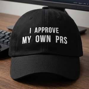 Könnte beinhalten: Eine schwarze Baseballkappe mit weißem, gesticktem Text auf der Vorderseite, der I APPROVE MY OWN PRS lautet. Die Kappe hat eine strukturierte Krone, einen gebogenen Schirm und einen Knopf an der Oberseite, was ein schlichtes Design ergibt.