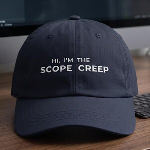 May include: A navy blue baseball cap featuring white embroidered text on the front that reads, "HI, I'M THE SCOPE CREEP." The cap has a structured crown, a curved brim, and a button at the top center, showcasing a clean and simple design.