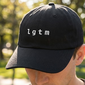 Può includere: Cappellino da baseball nero con visiera curva. Il cappellino presenta le lettere bianche "lgtm" ricamate sul davanti. Il cappello è realizzato in un tessuto morbido ed è indossato da una persona.
