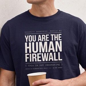 Peut inclure: Un t-shirt bleu marine à manches courtes avec un texte blanc imprimé : SECURITY AWARENESS MODULE 03 YOU ARE THE HUMAN FIREWALL ( this is not reassuring ) POSTED IN ACCORDANCE WITH POLICY 4.2 - DO NOT REMOVE. Le t-shirt possède un col rond.