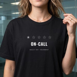 May include: A black short-sleeved t-shirt featuring a graphic with five star outlines, where only the first star is filled in. Below the stars, the text reads ON-CALL in white, followed by the smaller text would not recommend.