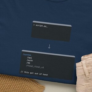 Puede incluir: Camiseta azul marino con un gráfico de un fragmento de código y el texto "script.py_". Debajo, se muestra otro fragmento de código con el texto "/system /api /auth /db /final_final_v3 // this got out of hand". La camiseta tiene cuello redondo y una etiqueta Comfort Colors.