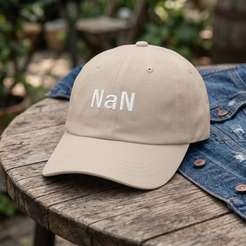 May include: A beige baseball cap featuring the text "NaN" embroidered in white thread on the front panel. The cap has a structured crown, a curved brim, and small ventilation eyelets at the top of each panel, presenting a clean and simple design.