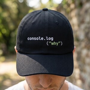 May include: Black baseball cap with the text "console.log ("why")" in white and green. The cap is made of a soft material and has a curved brim. A casual accessory for everyday wear.