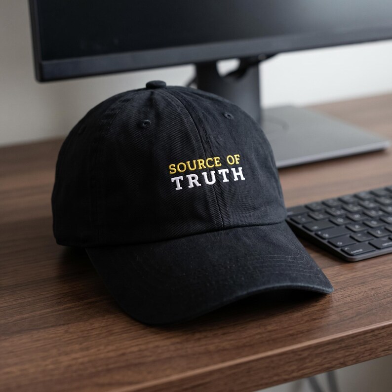 May include: A black baseball cap featuring the embroidered text "SOURCE OF" in yellow and "TRUTH" in white on the front panel. The cap has a structured crown, a curved brim, and a button at the top, showcasing a clean and simple design.