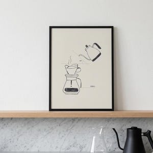 May include: Black framed print featuring a hand-drawn illustration of a pour-over coffee setup. The image shows a coffee maker, a kettle pouring water, and the text "300ml" and "45°". The background is a light beige color.