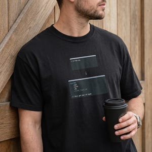 May include: Black t-shirt featuring a programming-themed graphic with code snippets and the text "script.py" and "// this got out of hand". The design includes a downward arrow and lines of code.