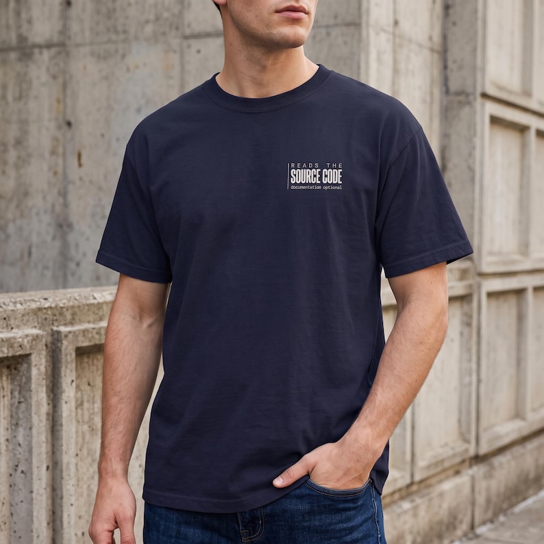 May include: A navy blue short-sleeved t-shirt featuring white text on the left chest that reads "READS THE SOURCE CODE" with the smaller text "documentation optional" underneath, all enclosed within a thin white rectangular border.