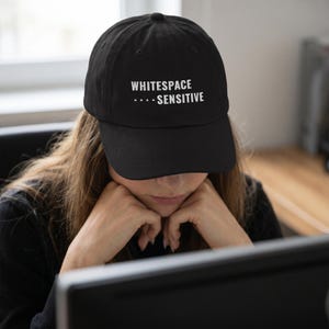 May include: A black baseball cap featuring the white embroidered text WHITESPACE SENSITIVE with four small dots preceding the word SENSITIVE. The cap has a structured crown, a curved brim, and a button at the top center of the fabric dome.