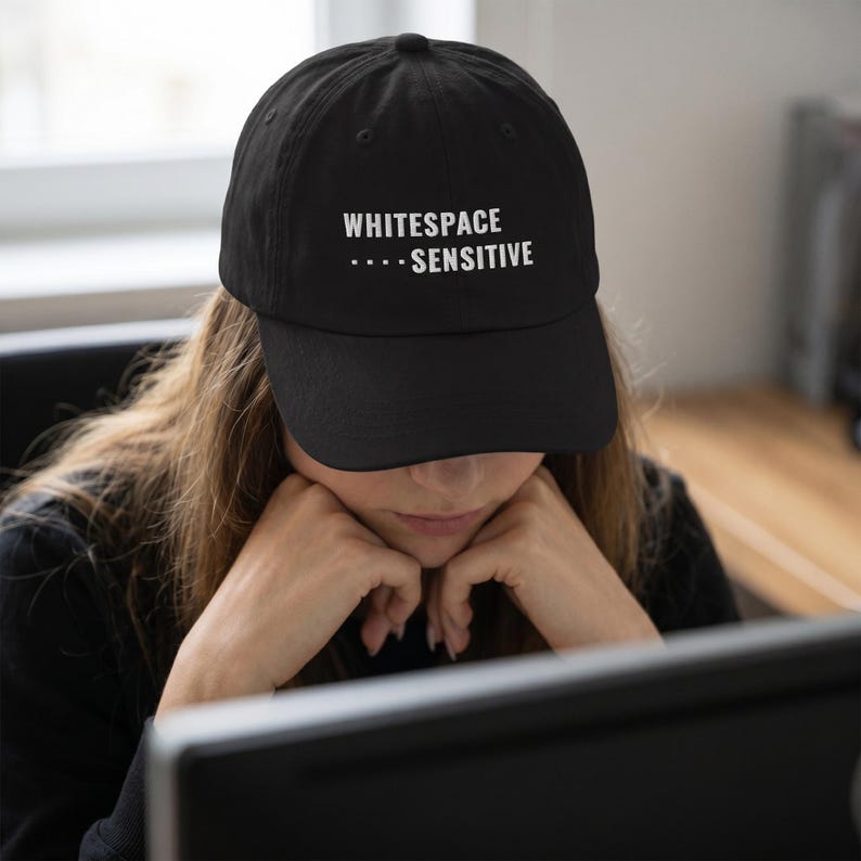 May include: A black baseball cap featuring the white embroidered text WHITESPACE SENSITIVE with four small dots preceding the word SENSITIVE. The cap has a structured crown, a curved brim, and a button at the top center of the fabric dome.