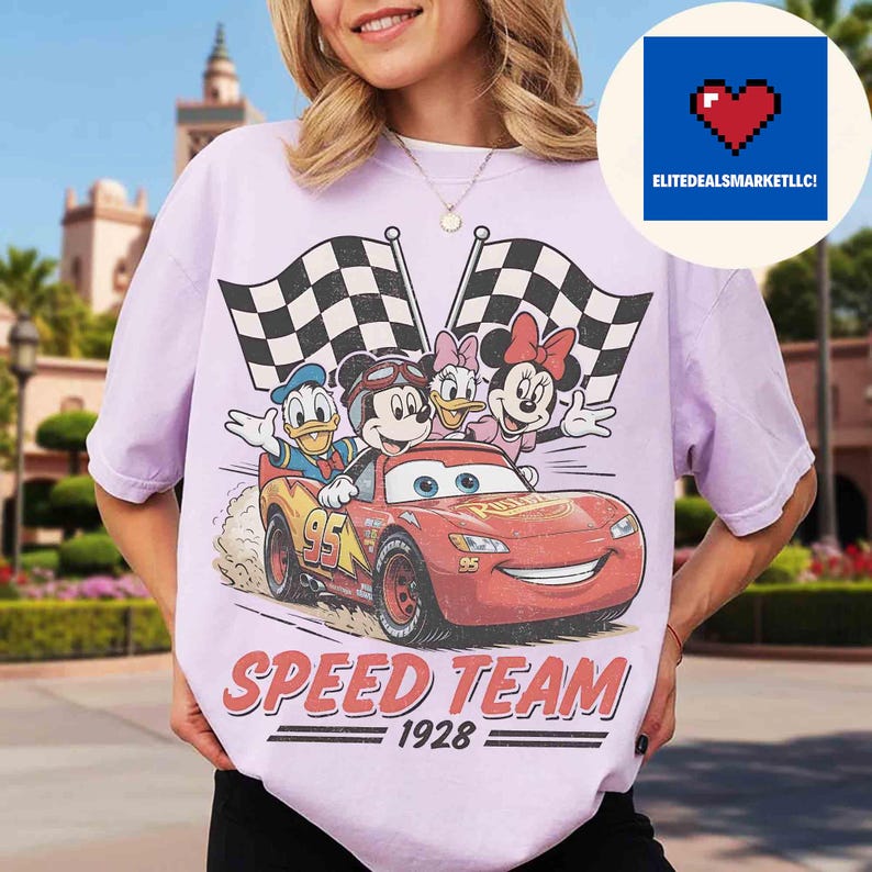 Pu&ograve; includere: Una maglietta lilla con una grafica di personaggi Disney su un'auto da corsa rossa, con bandiere a scacchi. Il testo "SPEED TEAM 1928" &egrave; stampato sotto. La maglietta &egrave; a girocollo.