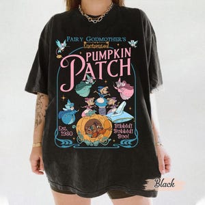 May include: Black t-shirt featuring a whimsical graphic of a pumpkin carriage with fairy godmothers and the text "Fairy Godmother's Enchanted Pumpkin Patch." The design includes the text "Est. 1950" and "Bibbidi Bobbidi Boo!"