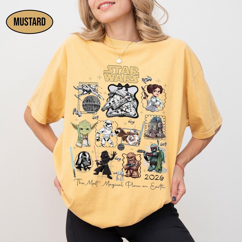 May include: Mustard-colored t-shirt featuring a Star Wars graphic with various characters and the text "2026 The Most Magical Place on Earth." The shirt has a crew neck and short sleeves.