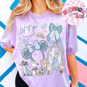 Może przedstawiać: Jasnofioletowa koszulka z nadrukiem graficznym z napisem "Let it go". Projekt zawiera obrazy księżniczki, płatk&oacute;w śniegu i postaci z kresk&oacute;wek. Koszulka ma kr&oacute;tkie rękawy.