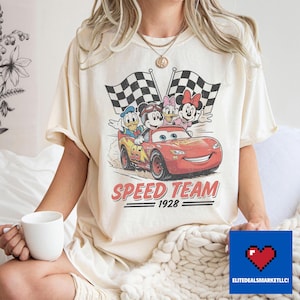 Pu&ograve; includere: T-shirt color crema con grafica in stile vintage di personaggi Disney su un'auto da corsa rossa con la scritta "SPEED TEAM 1928". Il design include Topolino, Paperino, Paperina e Minnie.