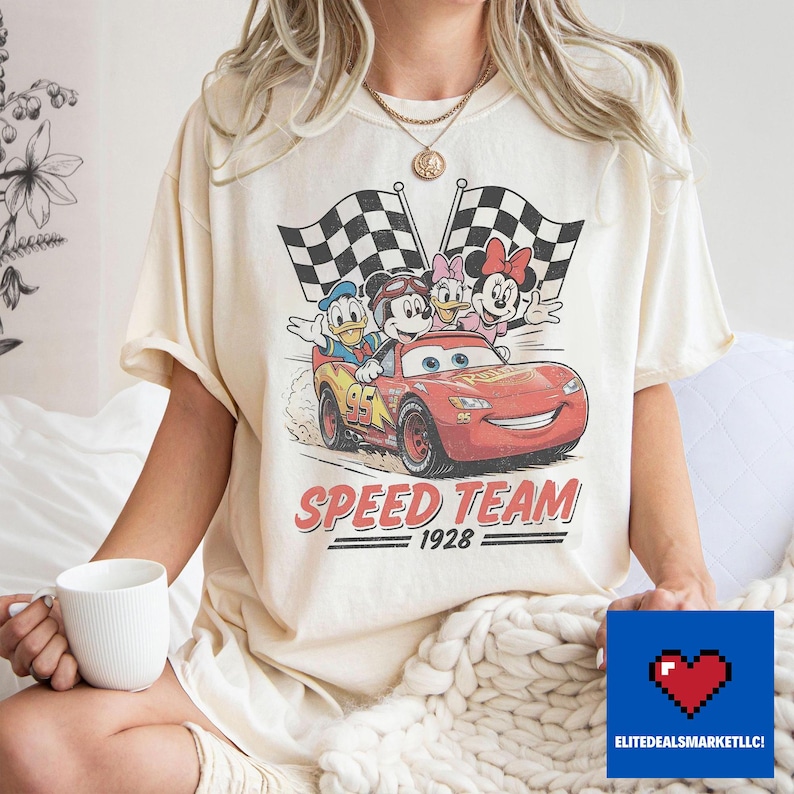 Pu&ograve; includere: T-shirt color crema con grafica in stile vintage di personaggi Disney su un'auto da corsa rossa con la scritta "SPEED TEAM 1928". Il design include Topolino, Paperino, Paperina e Minnie.