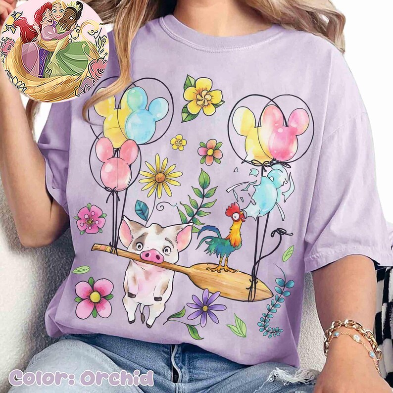 K&ouml;nnte beinhalten: Orchideenfarbenes T-Shirt mit einem skurrilen Design mit Zeichentrickfiguren, Blumen und Mickey Mouse-f&ouml;rmigen Ballons. Das Design umfasst ein Schwein, das ein Paddel h&auml;lt, einen Hahn und verschiedene florale Elemente. Das T-Shirt hat einen Rundhalsausschnitt.