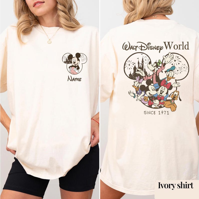 May include: An ivory t-shirt featuring a small Mickey Mouse graphic and the word Name on the front left chest. The back displays a large graphic of Disney characters, the text Walt Disney World, and the text Since 1971 inside a Mickey head.