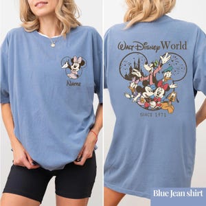 May include: A blue t-shirt featuring a graphic of Minnie Mouse on the front left chest with the word Name below it. The back displays a large graphic of Mickey Mouse, Minnie Mouse, Donald Duck, Daisy Duck, and Goofy with Walt Disney World text.