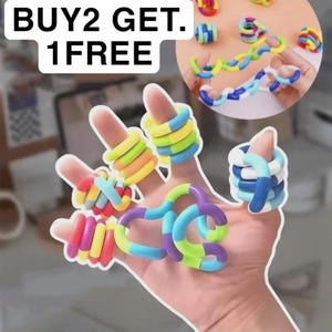 May include: A hand displaying colorful, interconnected fidget toys in various shapes and colors, including rings and linked segments. The image includes the text "BUY2 GET. 1 FREE".