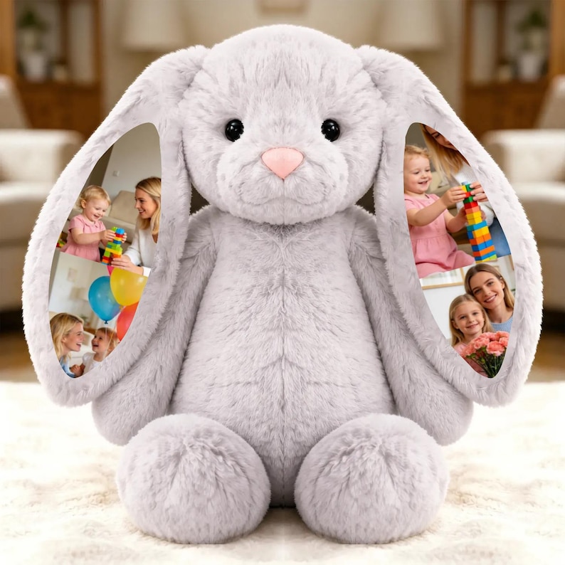 May include: A large, plush gray bunny rabbit stuffed animal with a pink nose and black eyes. The inside of each ear features a collage of family photos. The bunny is sitting on a white, fluffy surface.