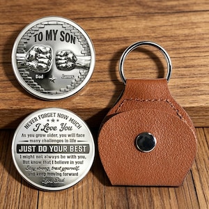 May include: A silver coin with the text "TO MY SON" and two fists. Below is the name "Dad" and "James". A second silver coin has the text "NEVER FORGET HOW MUCH I Love You" and a message. A brown leather keychain is also in the image.