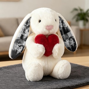 May include: A cream-coloured plush rabbit toy with long, floppy ears featuring black and white photo prints of couples. The rabbit has a soft, fuzzy texture, a small pink nose, and is holding a large, bright red plush heart between its paws.